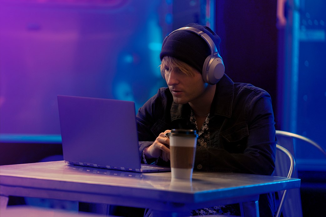 Image of a man with coffee wearing headphones and watchning his laptop