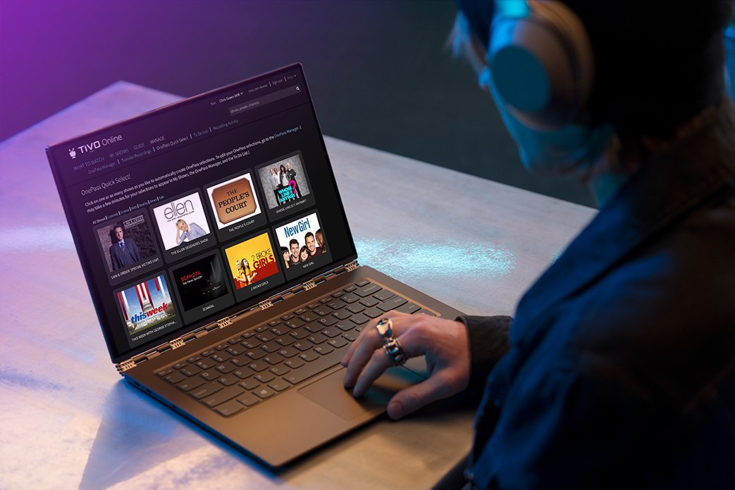 Image looking over the shoulder of a man wearing headphones using OnePass on his laptop