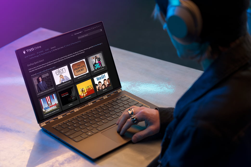 Image over-the-shoulder of a guy wearing headphones viewing TiVo Online on his laptop